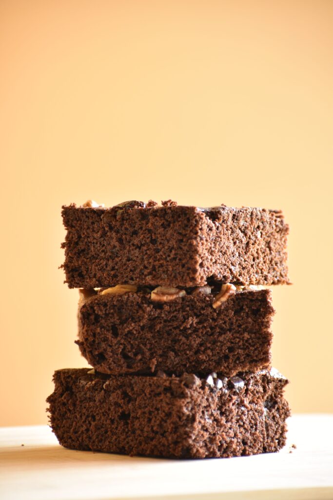 Three pieces of rich homemade chocolate brownies stacked on a wooden surface.